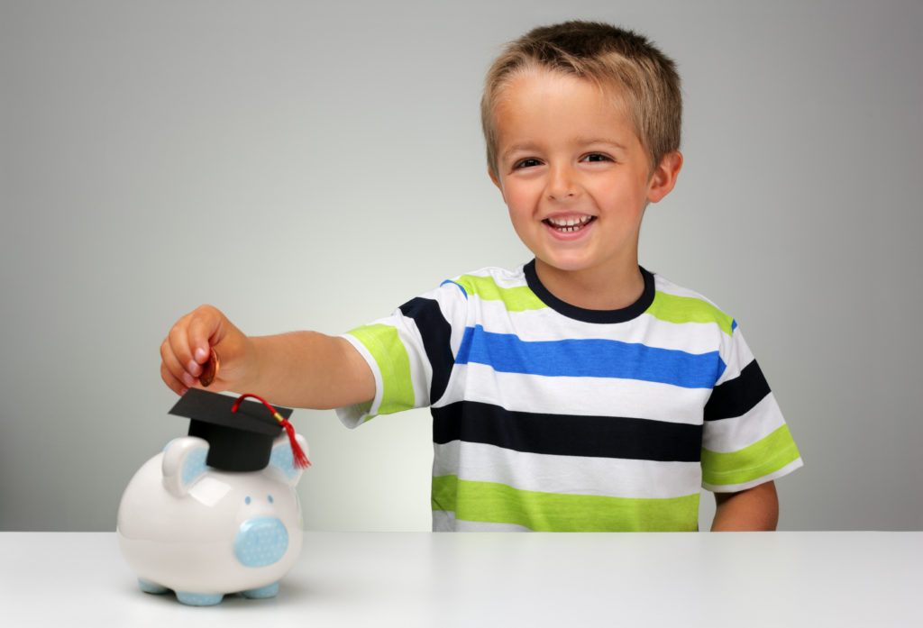 Young boy putting money into a piggy bank with a graduation mortar board cap concept for the cost of a college education