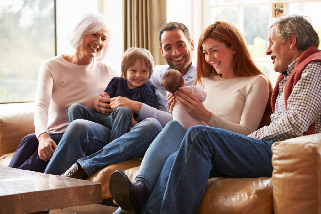 Multi Generation Family Sitting On Sofa With Newborn Baby